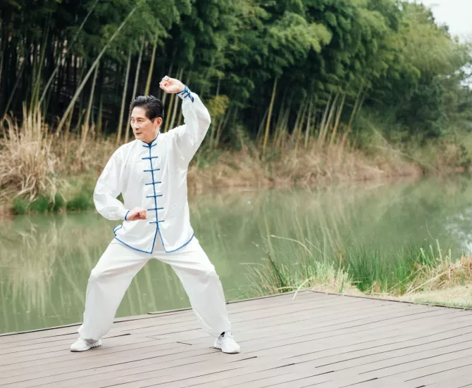 Asian senior man practicing tai chi outside by the river Asian senior man practicing tai chi outside by the river